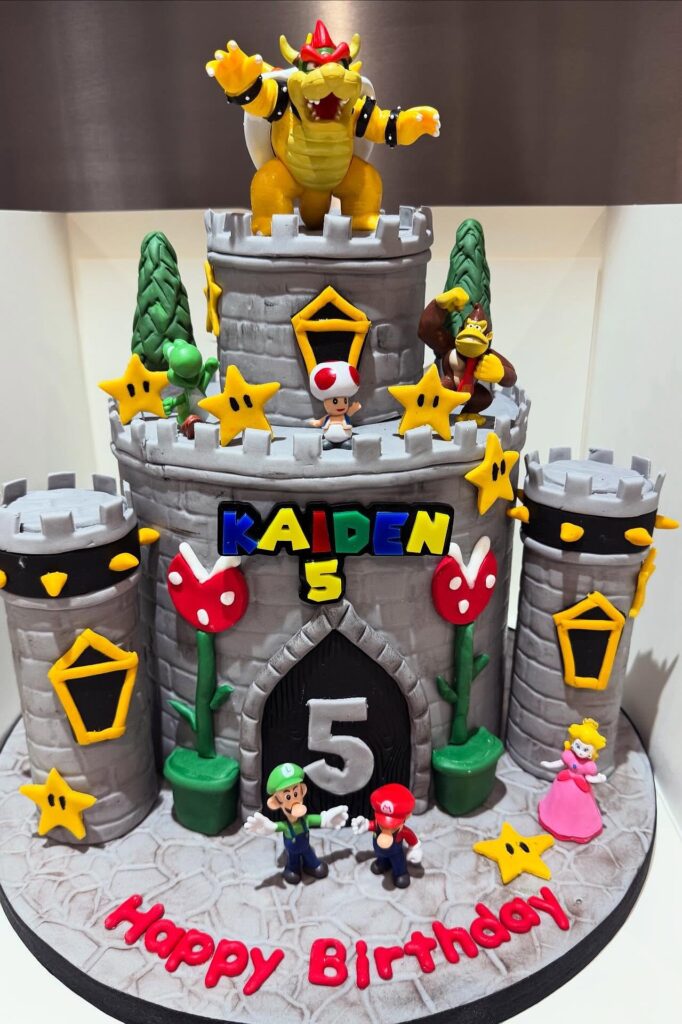 A colorful Bowser-themed birthday cake with Mario characters and castle decorations.