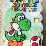 A colorful Yoshi-themed birthday cake with "Happy 5th Birthday Brian Jr." message, perfect for a Mar.