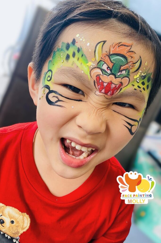 A colorful face painting of Bowser from Mario on a smiling boy's face, perfect for a birthday party.