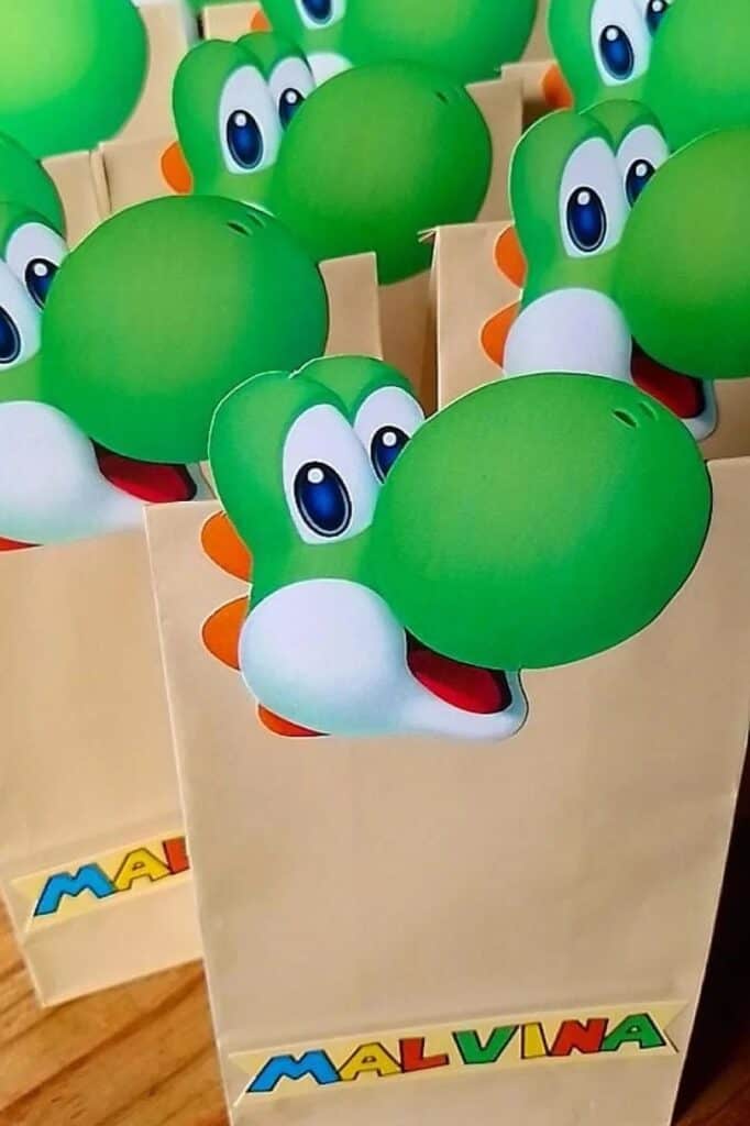 Yoshi-themed party favor bags with green dinosaur faces for a birthday celebration.