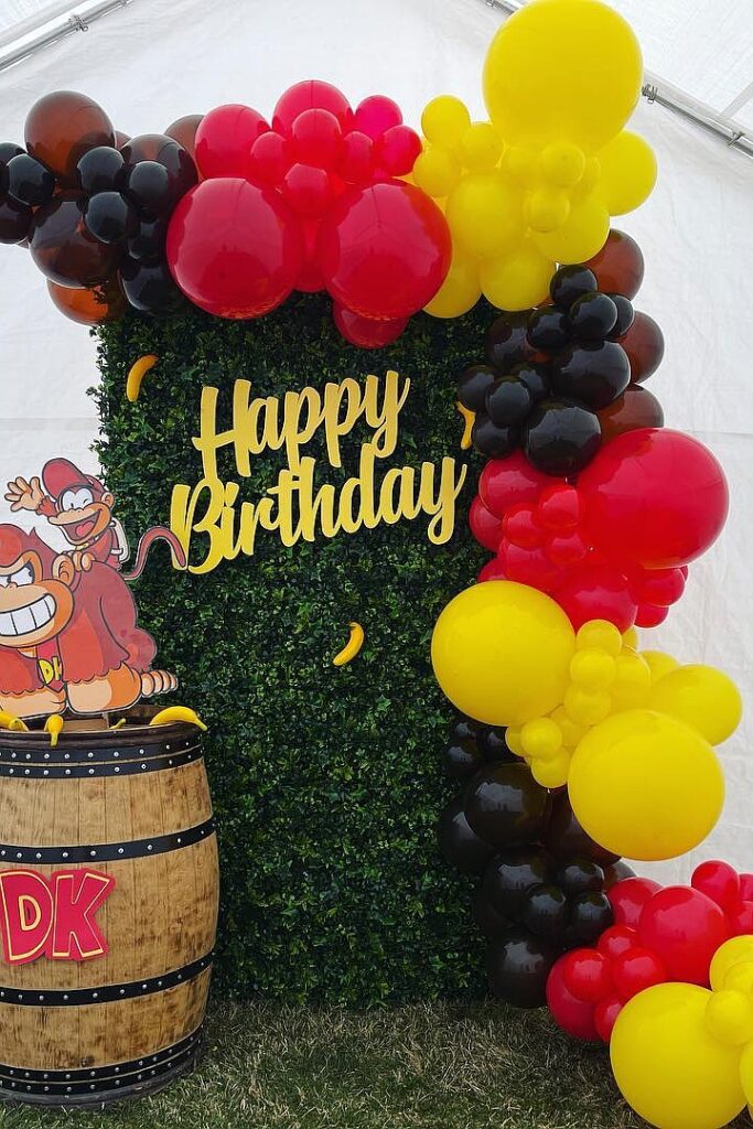 Happy Birthday balloon arch with Donkey Kong theme and greenery backdrop.