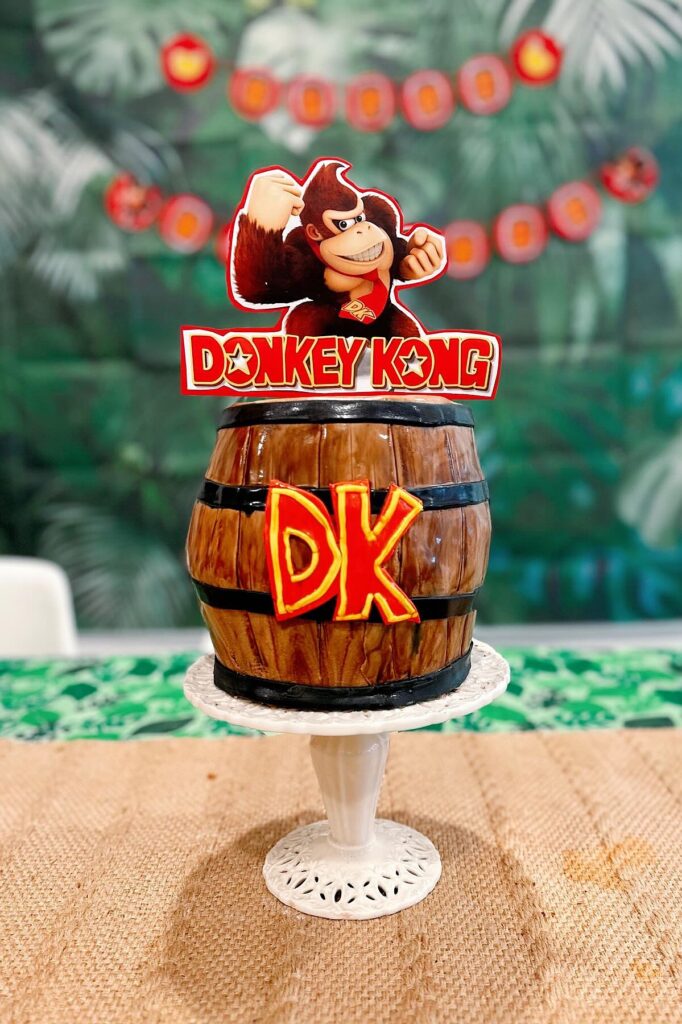 A colorful Donkey Kong themed birthday cake with DK logo and figurine on top, perfect for a party.