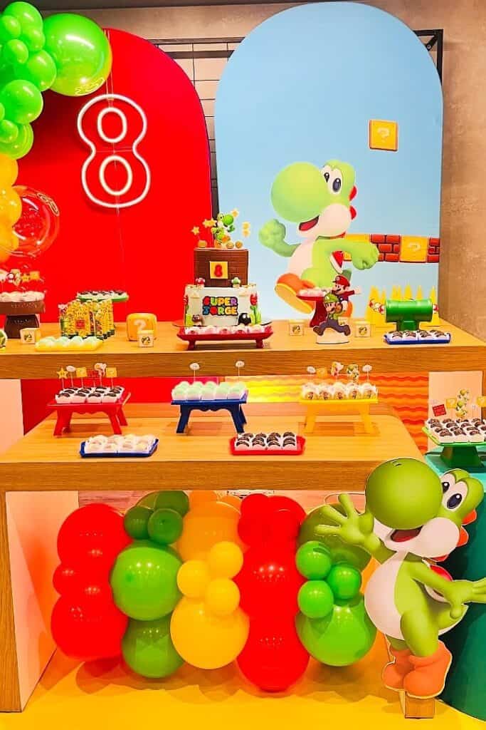A colorful Yoshi-themed birthday party setup with balloons, cake, and decorations.