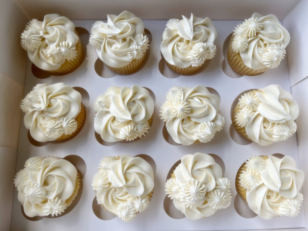 Elegant wedding cupcakes with white frosting and floral decorations in a box.