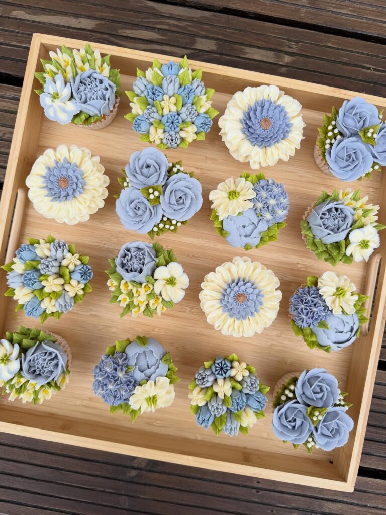 Elegant blue and white wedding cupcakes with floral decorations on wooden tray.