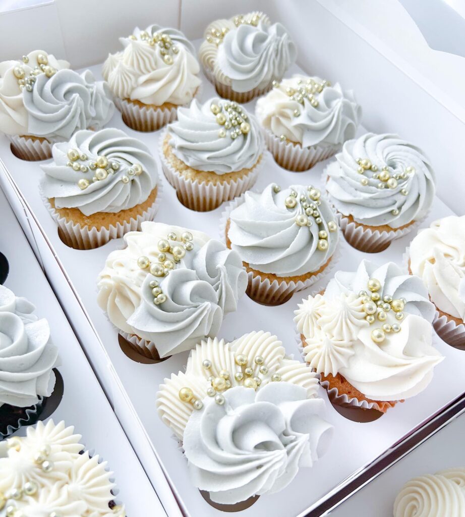 Elegant wedding cupcakes with white frosting and pearl decorations on a white tray.