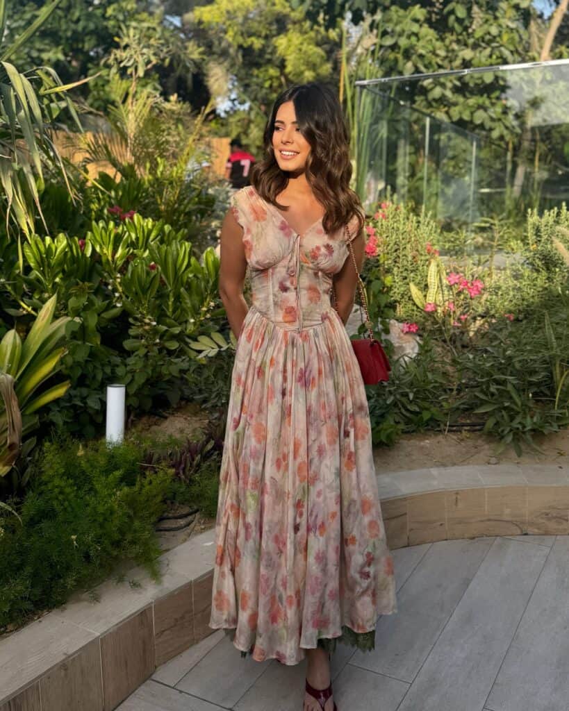 Elegant woman in floral maxi dress standing in lush garden setting.