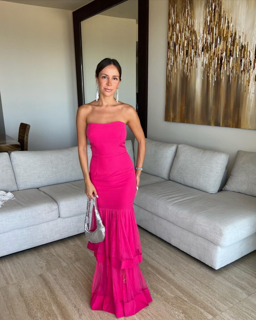 Elegant woman in a bright pink strapless gown standing in modern living room with artwork and sofa.