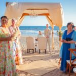 Wedding ceremony on a sandy beach with guests watching.