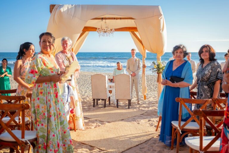 Wedding ceremony on a sandy beach with guests watching.