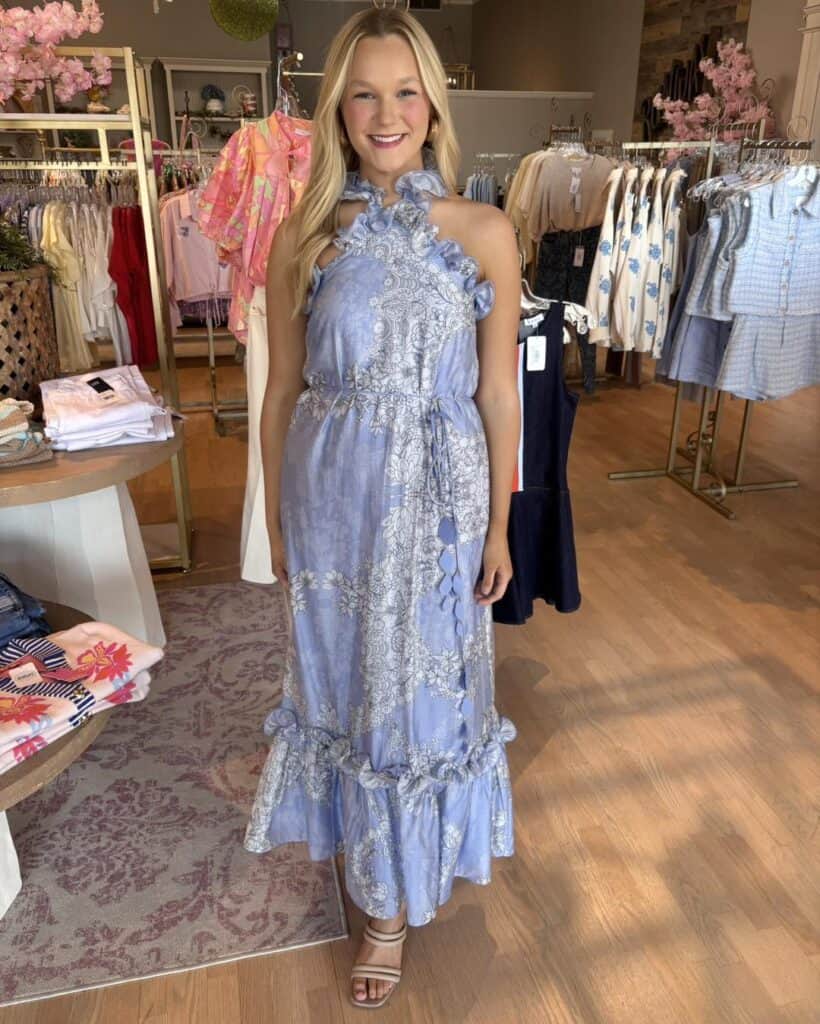 A woman in a blue floral maxi dress shopping at Confetti & Roses boutique.