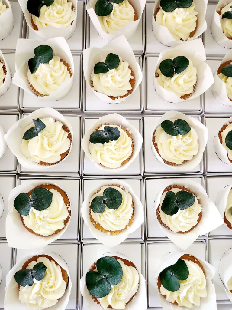 Assorted wedding cupcakes with white frosting and green leaves on top, arranged in rows.