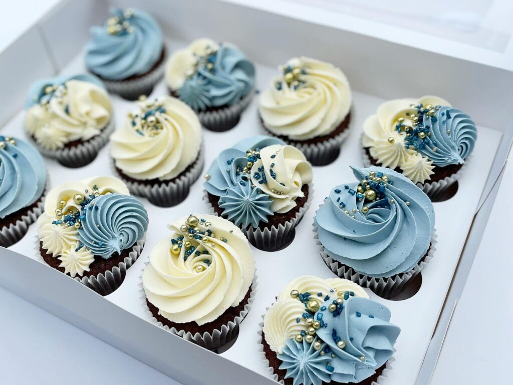 Assorted wedding cupcakes with blue and white frosting and decorative pearls in a box.