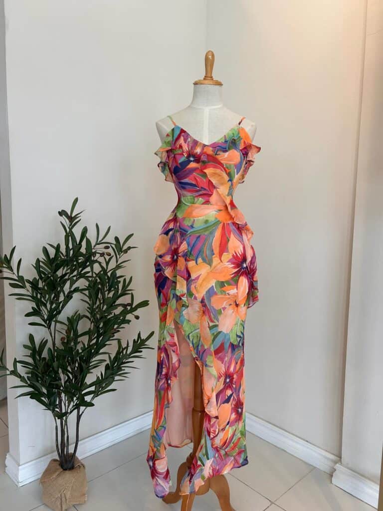A colorful floral maxi dress displayed on a mannequin with a potted plant nearby.