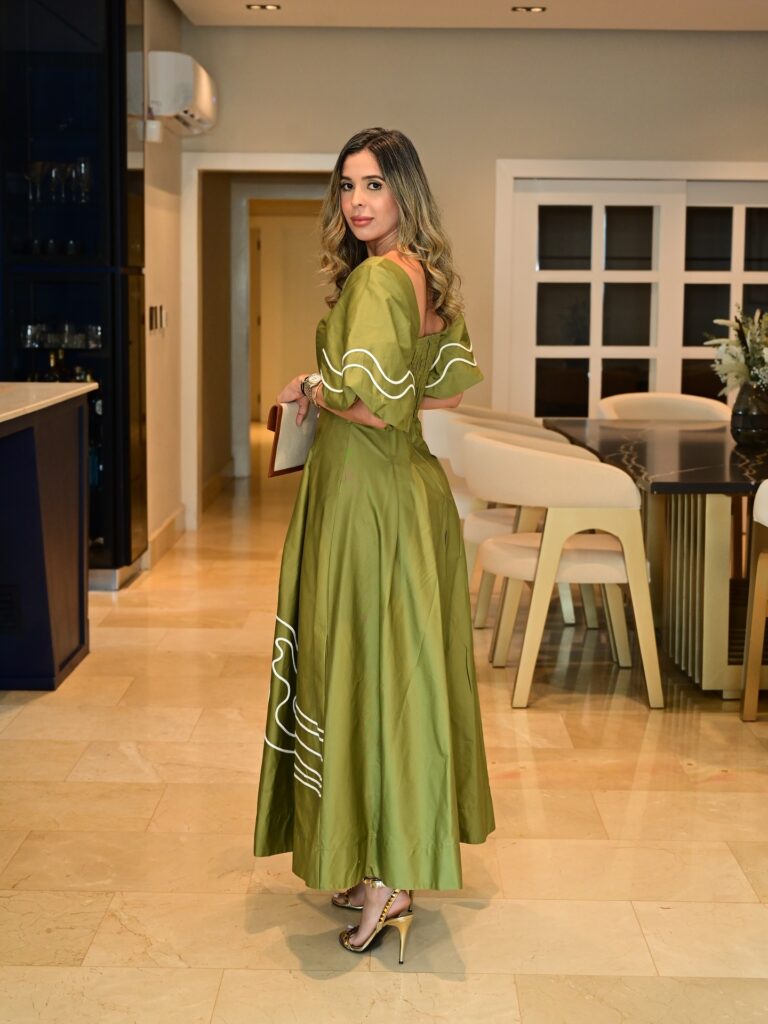A woman in a green dress standing in a modern living room with dining area.