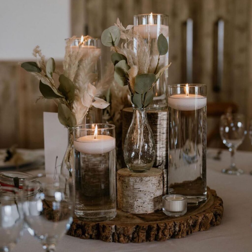 Elegant floating candle wedding centerpieces with greenery on rustic wood base.