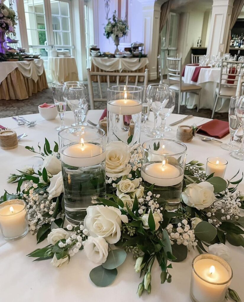 Elegant wedding centerpiece with floating candles, white roses, and greenery.