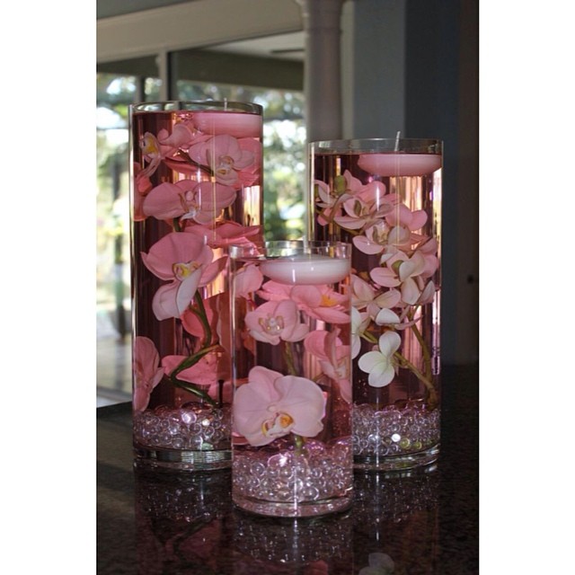 Floating candles with pink orchids in tall glass vases for wedding decor.