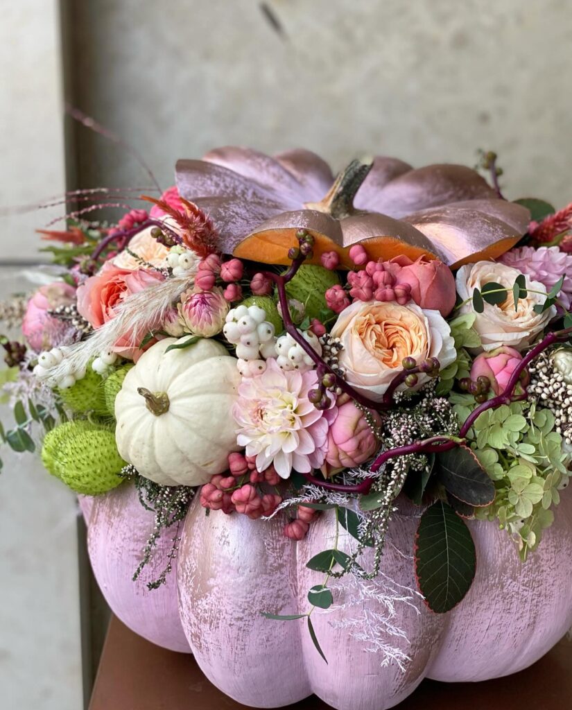 Elegant pumpkin centerpiece with roses, berries, and greenery for wedding decor.