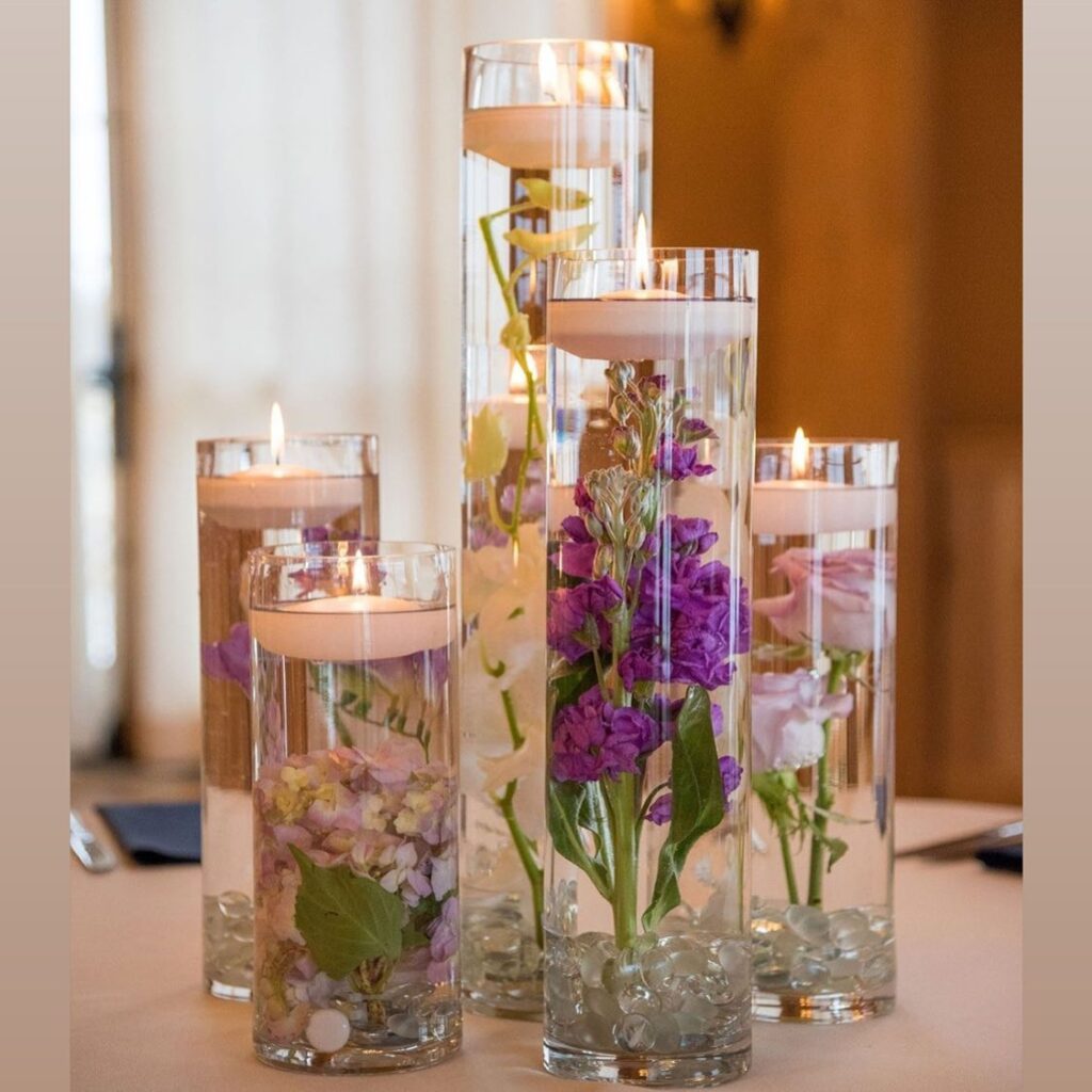 Floating candle wedding centerpieces with purple flowers in tall glass vases for reception decor.