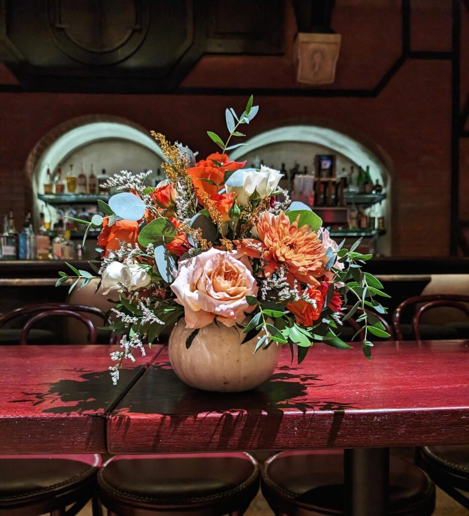 Elegant fall floral arrangement with roses, chrysanthemums, and greenery in a beige vase.