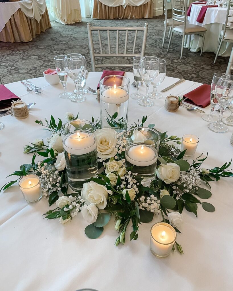 Elegant wedding table centerpiece with floating candles and white roses for reception decor.