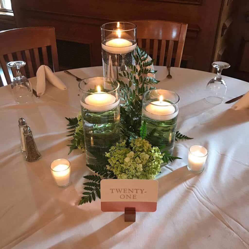 Elegant floating candle centerpiece with greenery and table number at wedding reception.