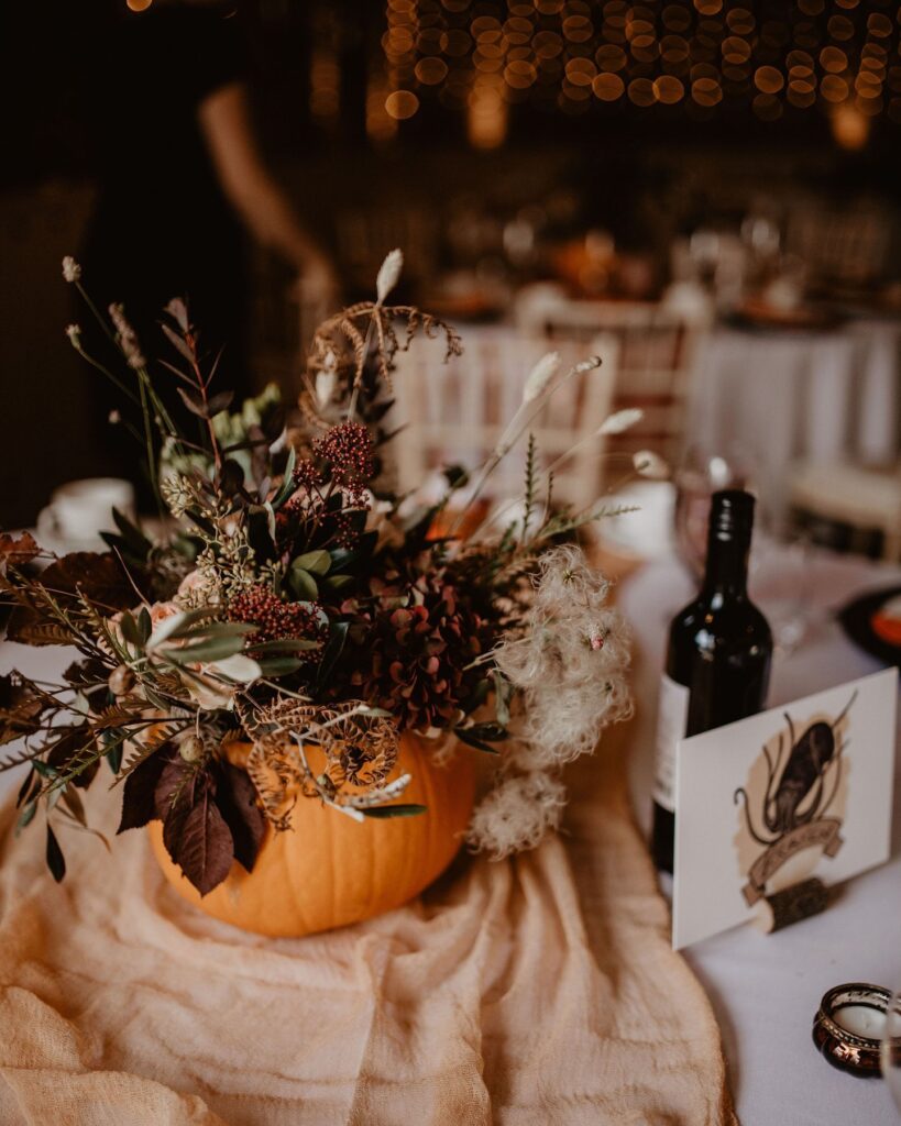Elegant pumpkin centerpiece with fall flowers and candles for wedding decor.