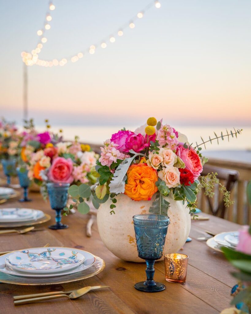 Elegant wedding table centerpiece with vibrant pink, orange, and peach flowers by the beach.