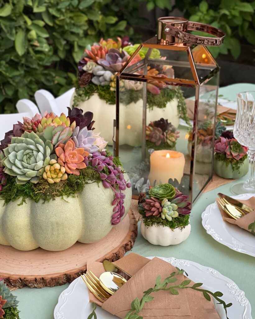 Elegant pumpkin wedding centerpiece with succulents and candles on a garden table.