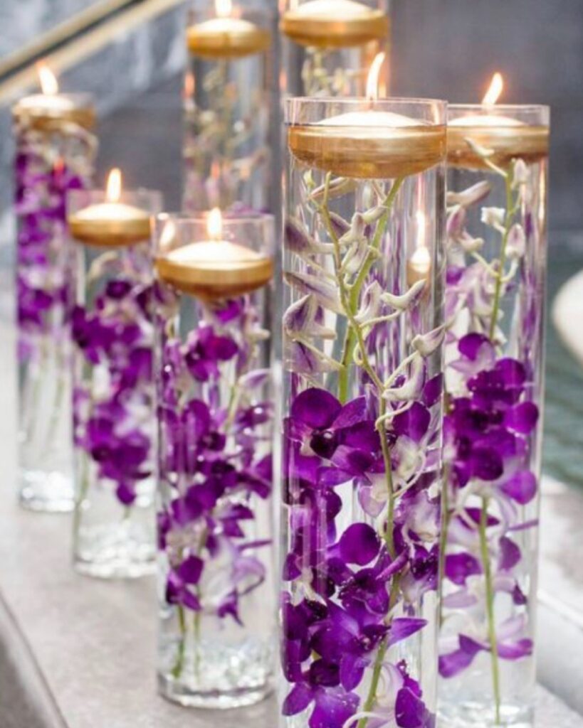 Floating candle wedding centerpieces with purple orchids in tall glass vases.