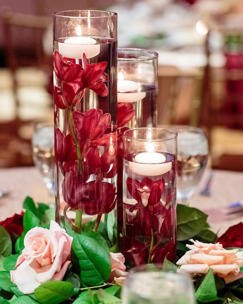 Floating candle wedding centerpieces with red flowers and roses for reception decor.