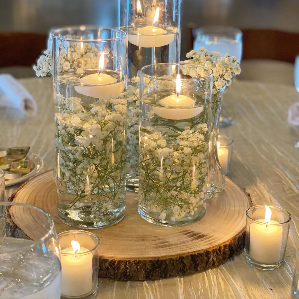 Floating candles and white flowers in glass vases on wooden slab for wedding decor.