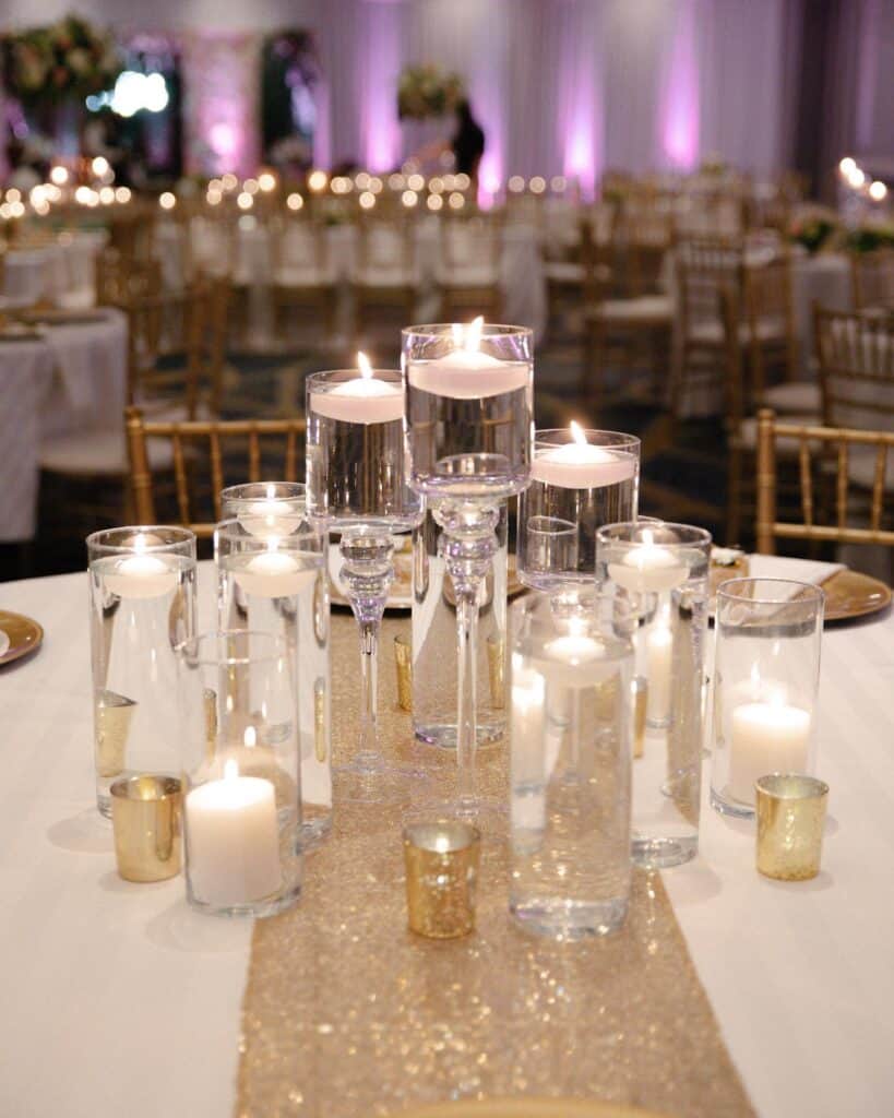 Elegant wedding reception table with floating candles in glass holders and gold accents.