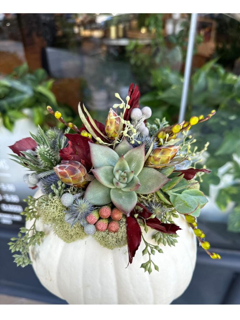 Elegant pumpkin centerpiece with succulents, berries, and foliage for fall weddings.