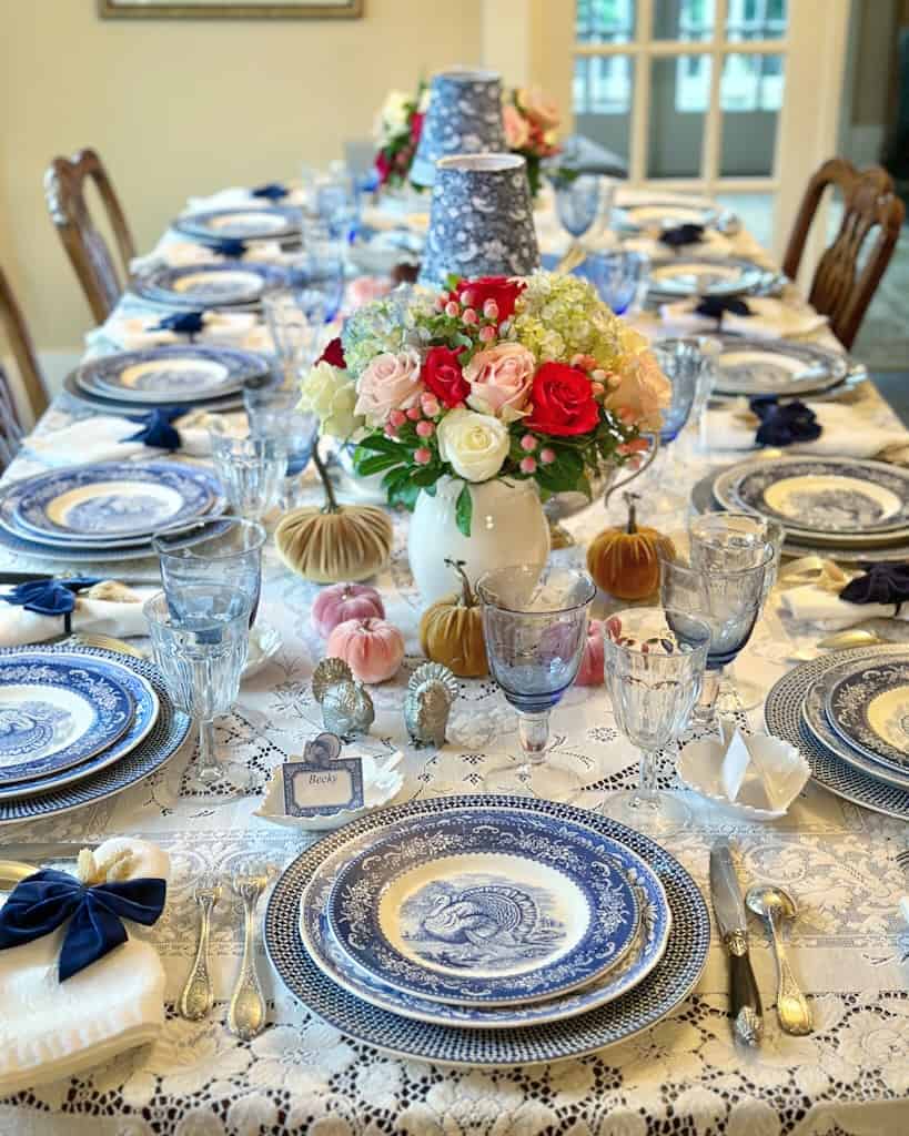Elegant Thanksgiving table setting with blue and white china, floral centerpiece, and pumpkins.