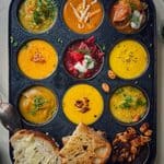 Assorted mini soups in a black tray with bread and toppings for cozy party dining.