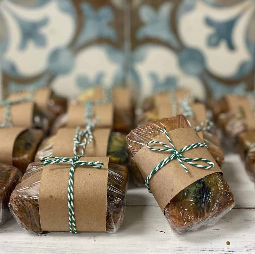 Wrapped homemade soap bars with brown paper and green striped twine on a rustic surface.