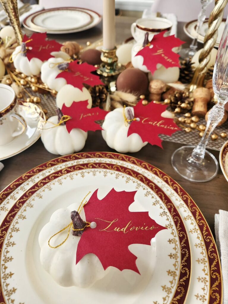 Elegant Thanksgiving table setting with pumpkin-shaped desserts and autumn leaf decorations.