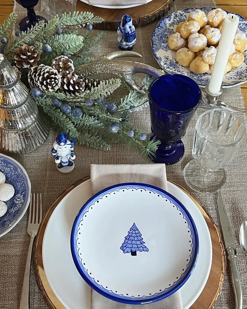 Festive holiday table setting with blue and white Christmas-themed dinnerware and decorations.