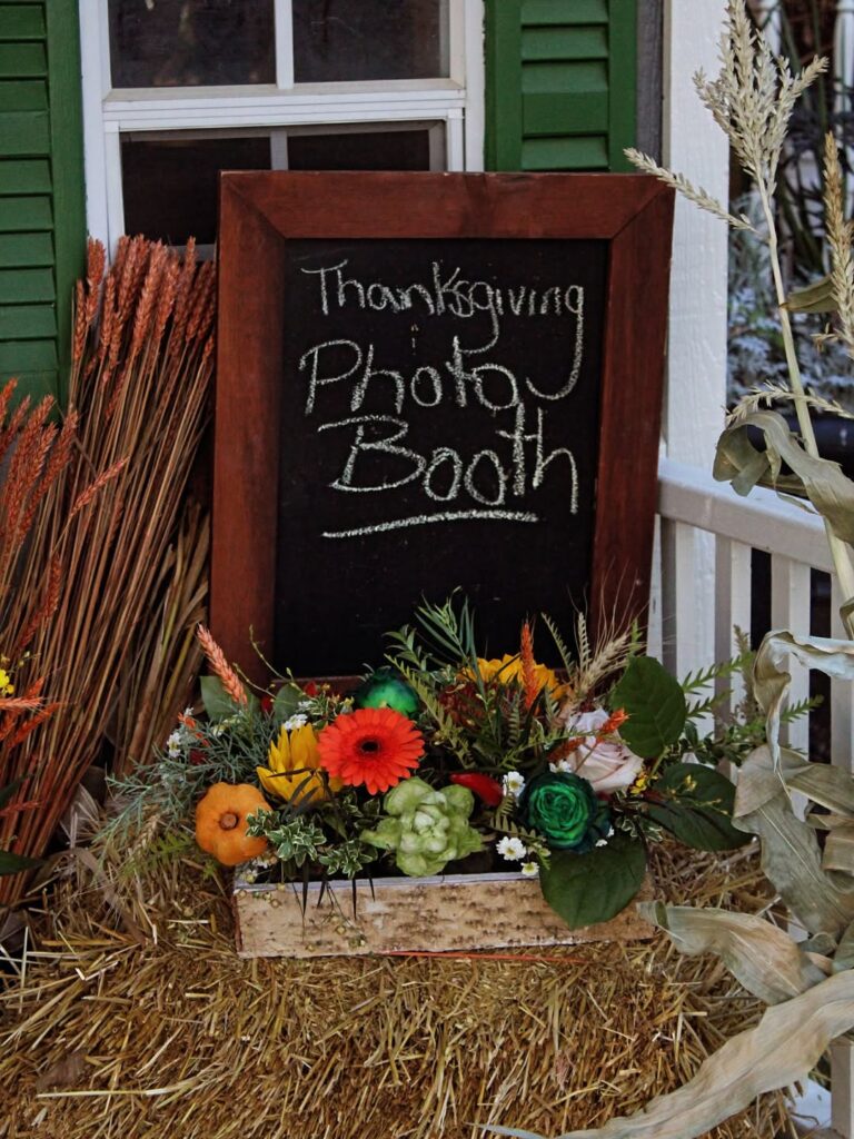 Thanksgiving photo booth sign with fall floral decorations and hay bale backdrop.