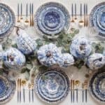 Blue and white Thanksgiving table setting with pumpkins, eucalyptus, and gold cutlery.