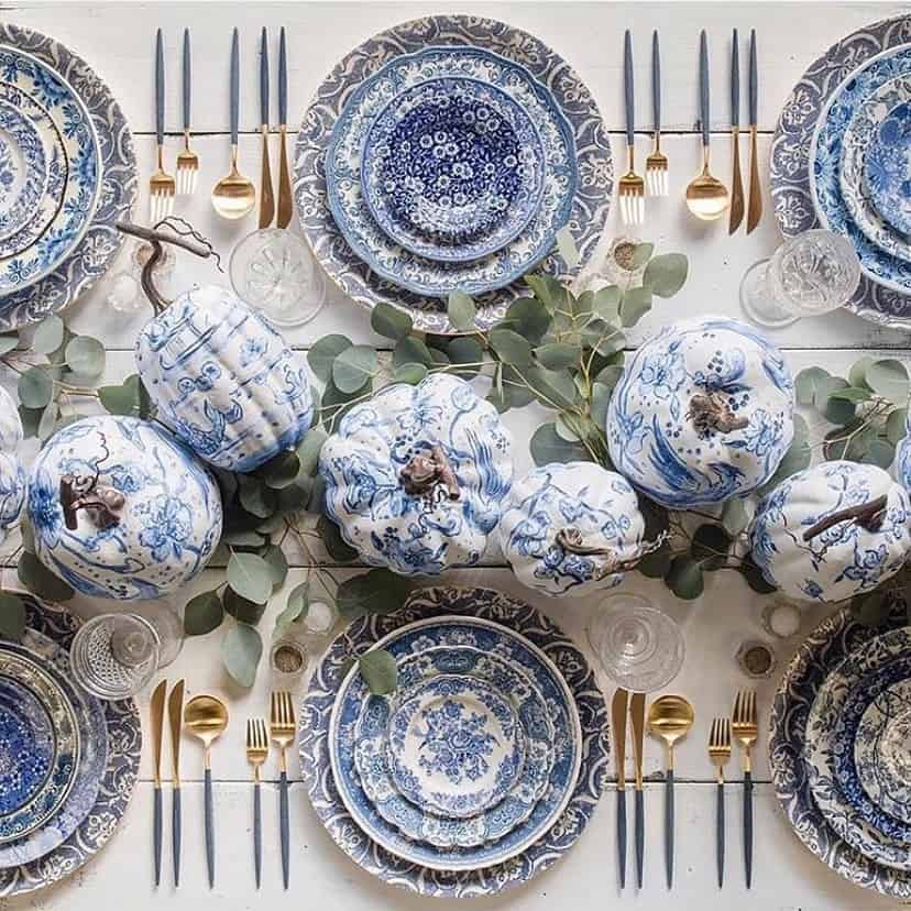 Blue and white Thanksgiving table setting with pumpkins, eucalyptus, and gold cutlery.