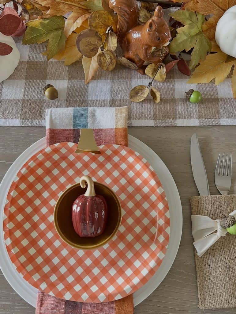 Autumn-themed table setting with a small pumpkin on a checkered plate for fall gathering.