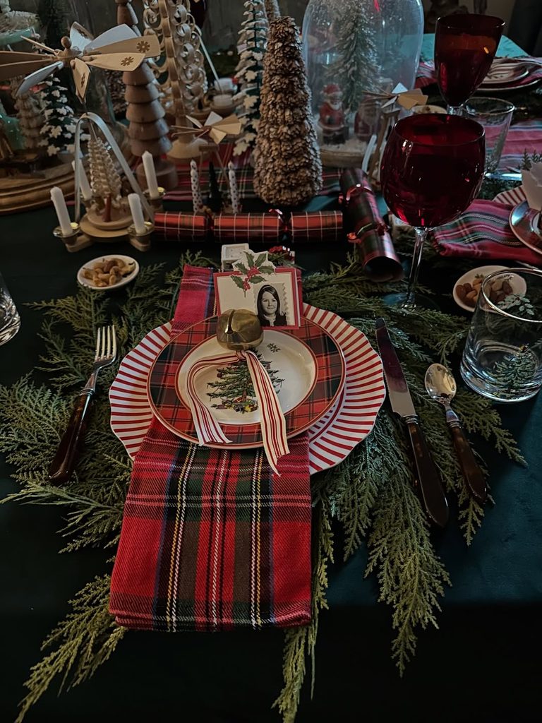 Festive Christmas table setting with plaid napkin, holiday decor, and red wine glasses.