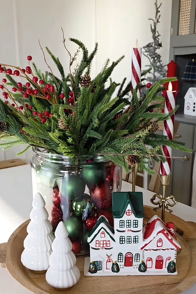 Festive Christmas centerpiece with pine branches, red berries, candles, and holiday decorations.