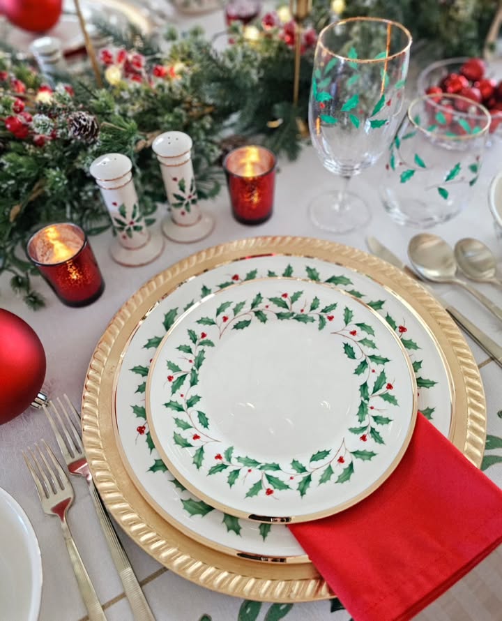 Festive Christmas table setting with holly-themed plates, candles, and holiday decor.