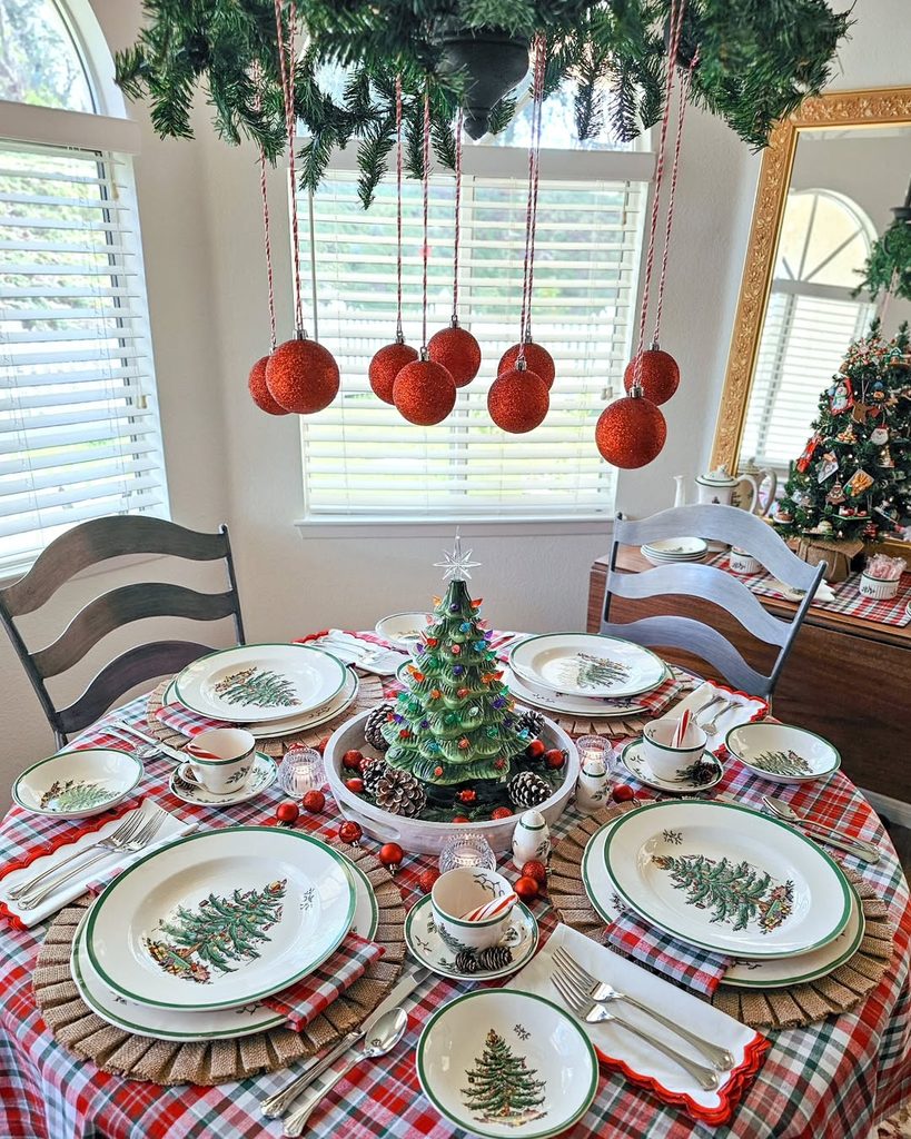 Festive Christmas table setting with decorated tree, hanging ornaments, and holiday decor.