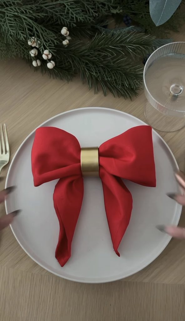 Festive holiday table setting with red napkin bow and gold napkin ring.