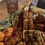 Thanksgiving table with corn, olives, bread, and decorative foliage for festive gathering.